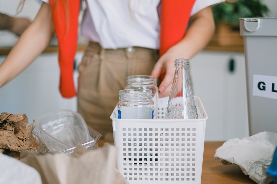A clear glass soda bottle with embossed branding, positioned vertically on a wooden surface, partially surrounded by crumpled white paper and other miscellaneous waste materials. The bottle's surface